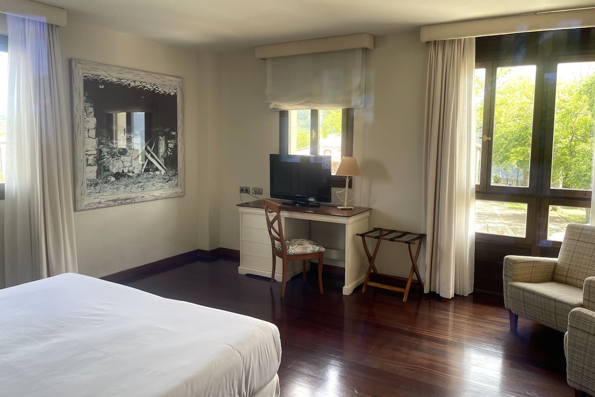 Une chambre d’hôtel avec un lit, un bureau avec une télévision, une chaise et une fenêtre avec des rideaux.