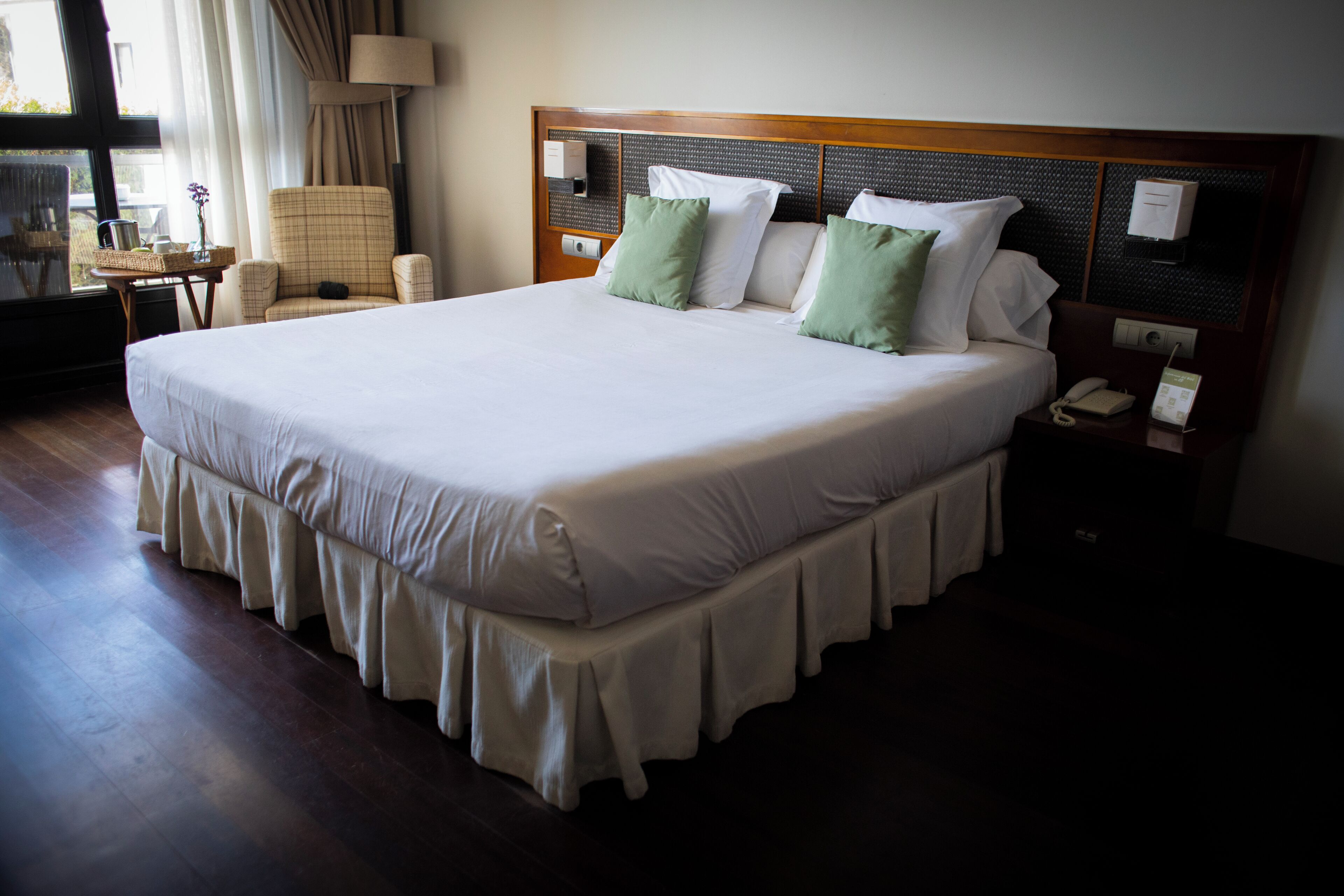 Una cama grande con cabecera de madera, una mesita de noche con lámpara y una silla.