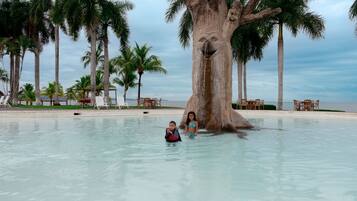 Relax by the serene pool surrounded by palm trees and a unique rock formation.