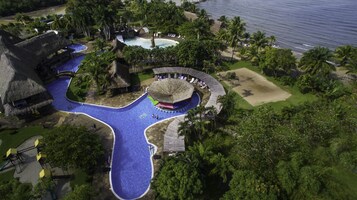 An aerial view of a resort with multiple swimming pools, a beach area, and lush greenery.