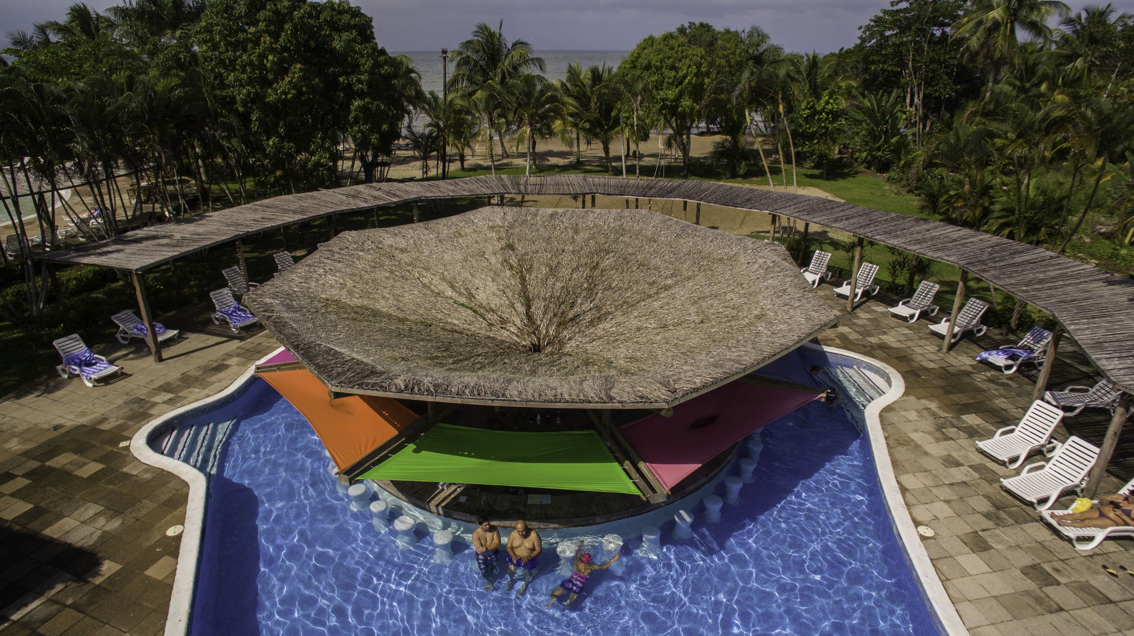 Una piscina rodona amb una illa al centre, envoltada de gandules i zones d'estar cobertes.