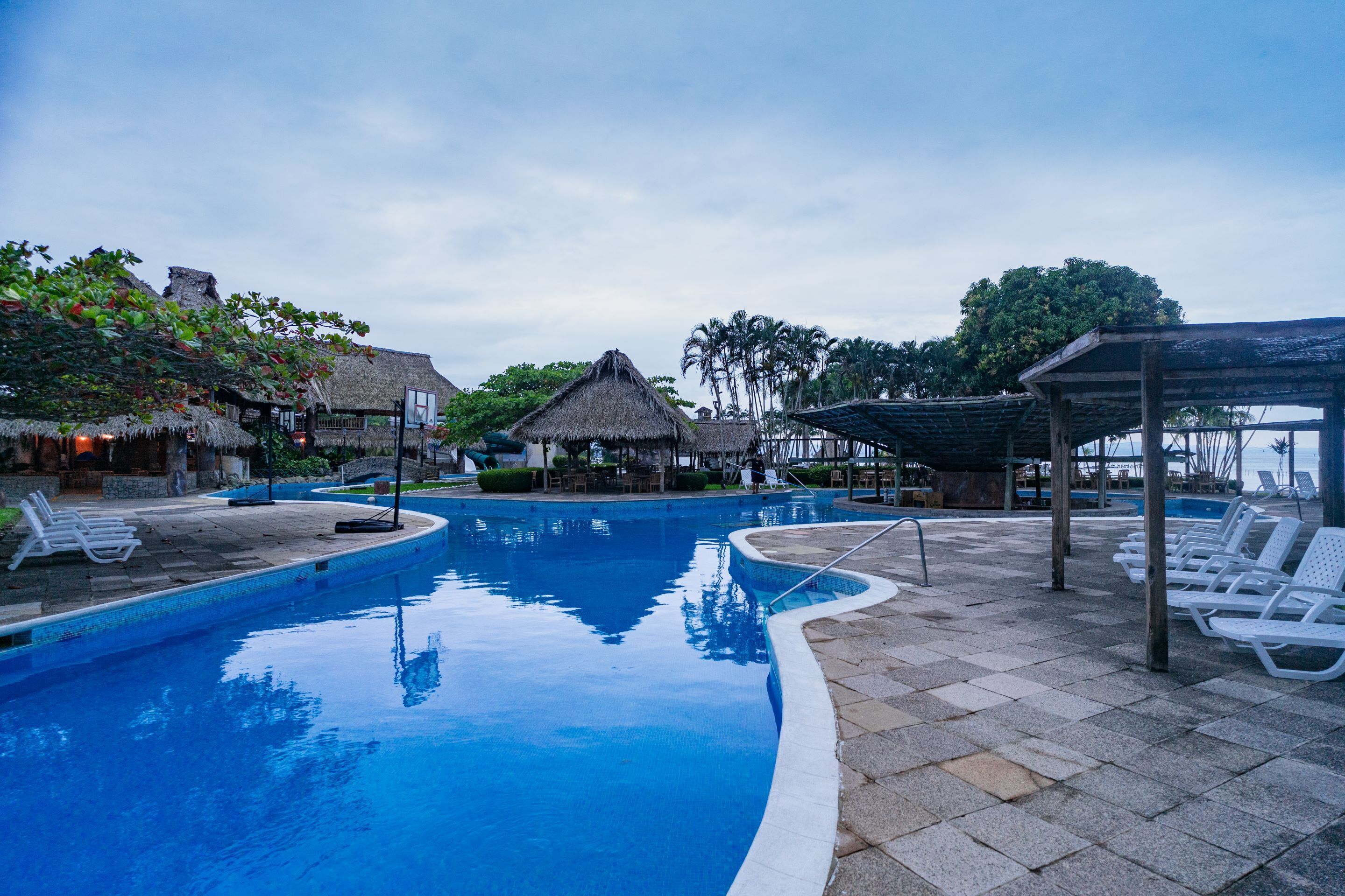 A swimming pool with lounge chairs and thatched-roof structures.