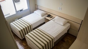 Habitación de hotel con dos camas individuales, cada una con colcha a rayas, una mesita de noche con teléfono y una ventana que da a la calle.