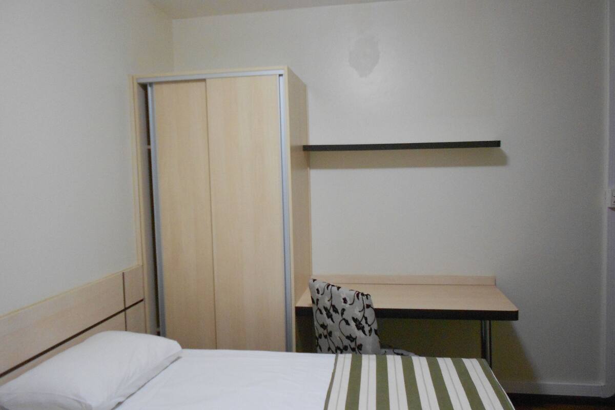 A bedroom with a bed, a wardrobe, a desk, and a chair.