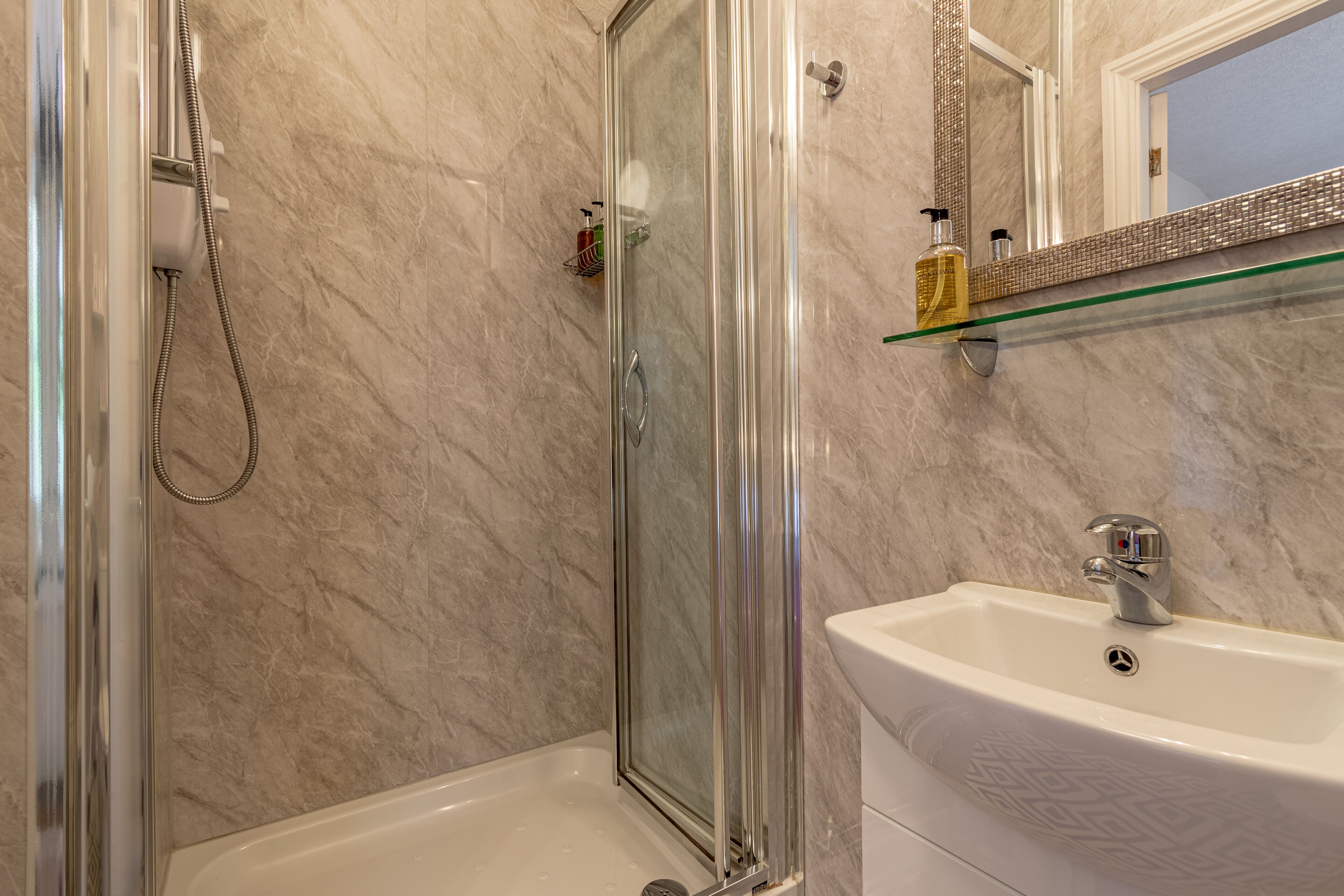 A bathroom with a glass-enclosed shower, a white sink, and a marble-tiled wall.