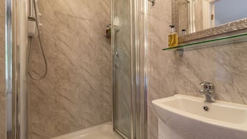 A bathroom with a glass-enclosed shower, a white sink, and a marble-tiled wall.
