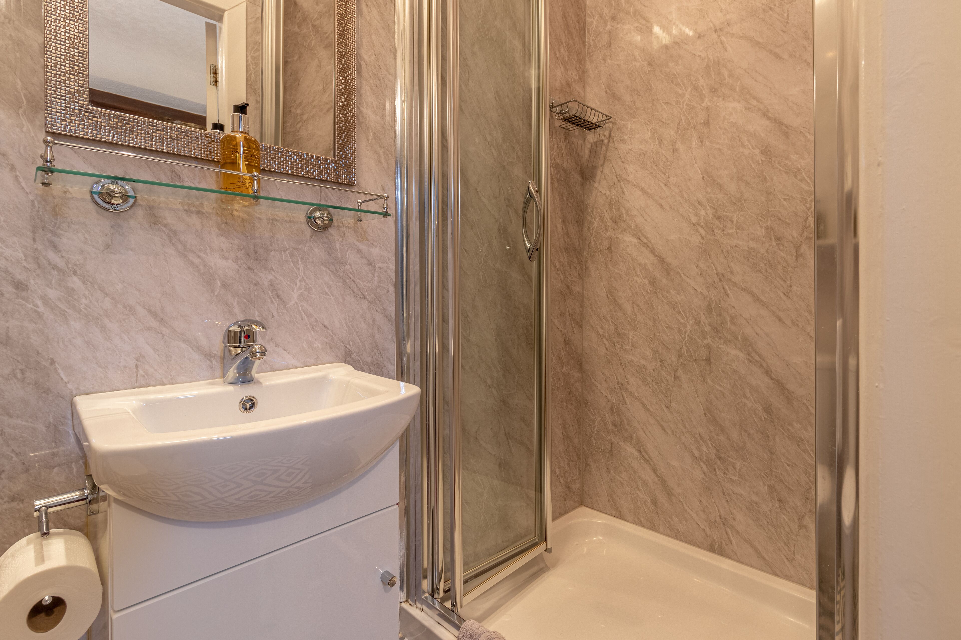 A bathroom with a glass shower enclosure, a white sink, and a marble-tiled wall.