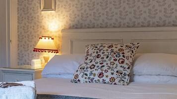 Cama bem arrumada com almofadas florais, duas luminárias de cabeceira e papel de parede estampado.