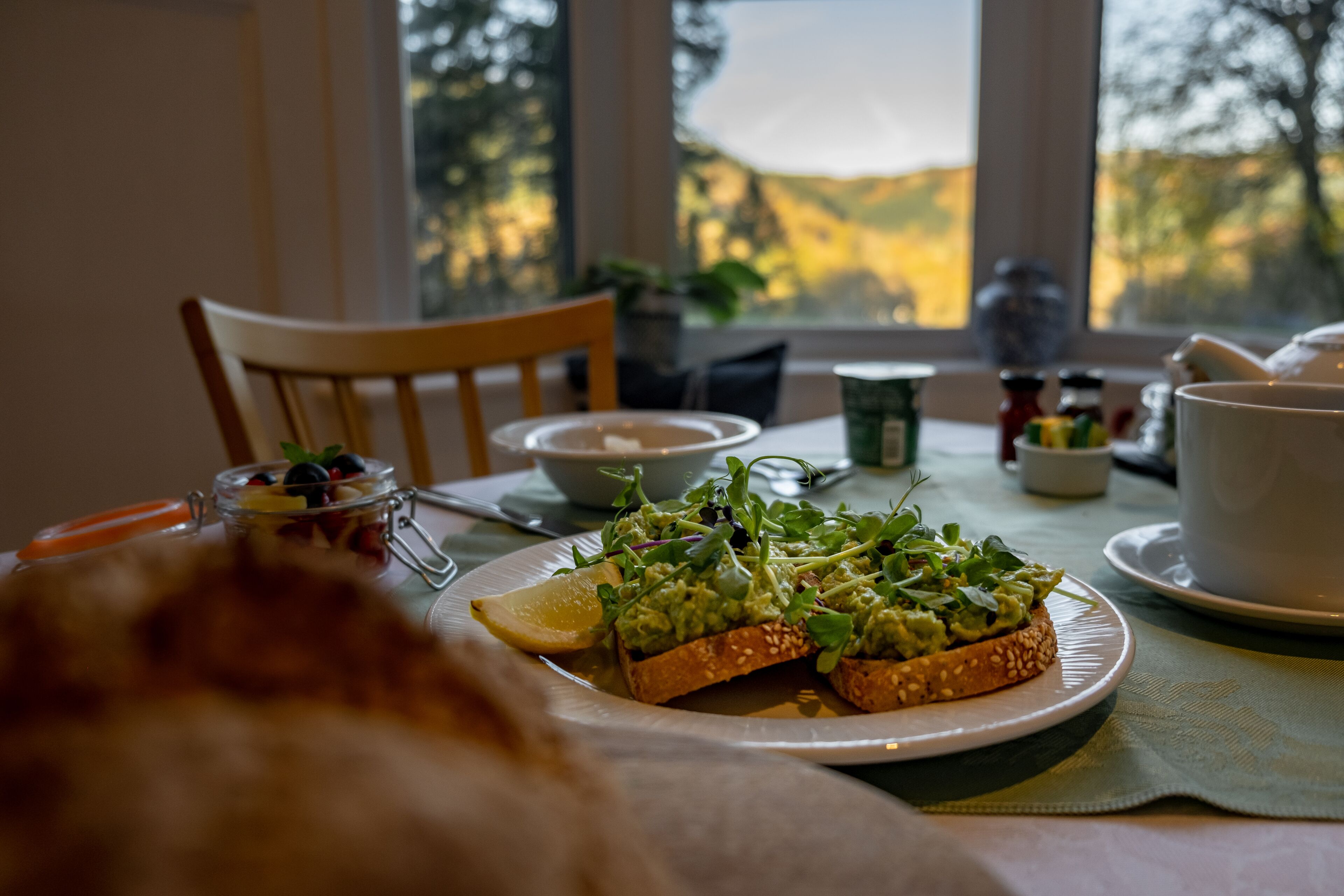 A dining table with a plate of avocado toast, a bowl, and a cup.
