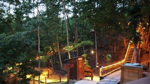 Une terrasse en bois avec un escalier menant à une petite construction en bois, entourée d’arbres et éclairée d’une lumière chaleureuse.