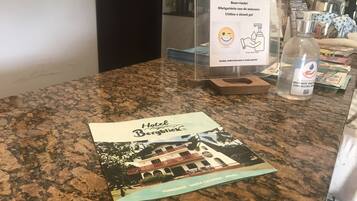 Un folleto de hotel sobre un mostrador, con una vitrina de plástico que muestra un cartel sobre el uso obligatorio de mascarillas y gel hidroalcohólico.