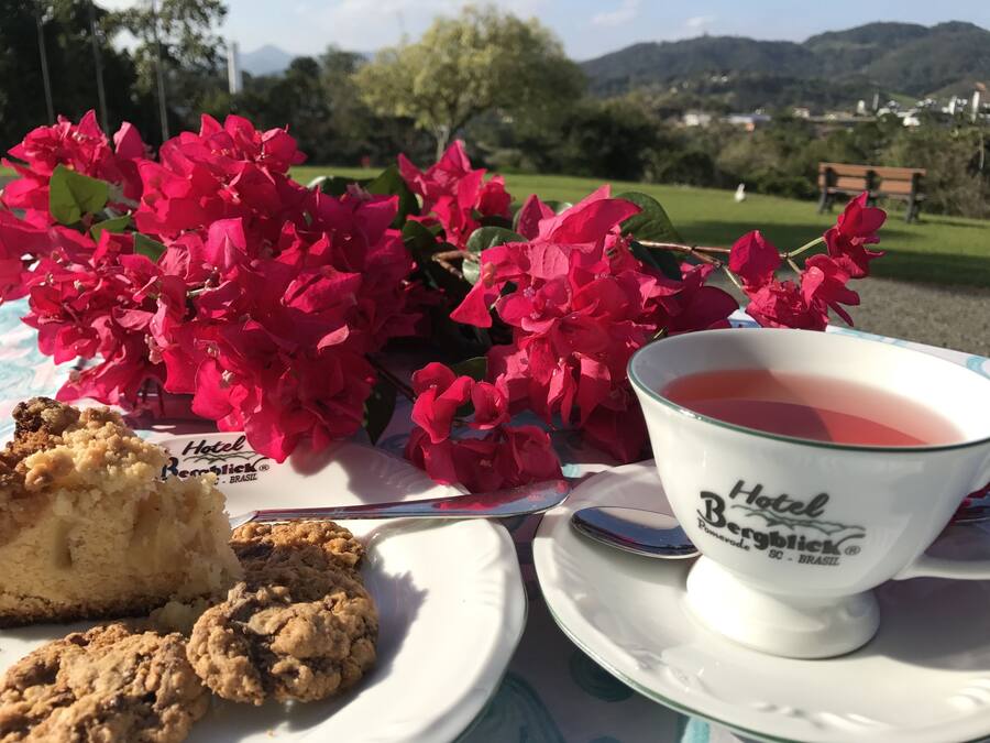 A table with a slice of cake, a cup of tea, and pink flowers.