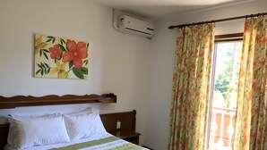 A bedroom with a bed, a painting of flowers, an air conditioning unit, and a balcony with curtains. - Hotel Bergblick (Pomerode)
