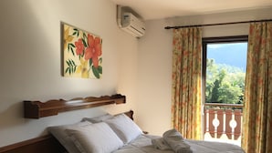 A bedroom with a bed, a painting, an air conditioner, and a view of greenery outside. - Hotel Bergblick (Pomerode)