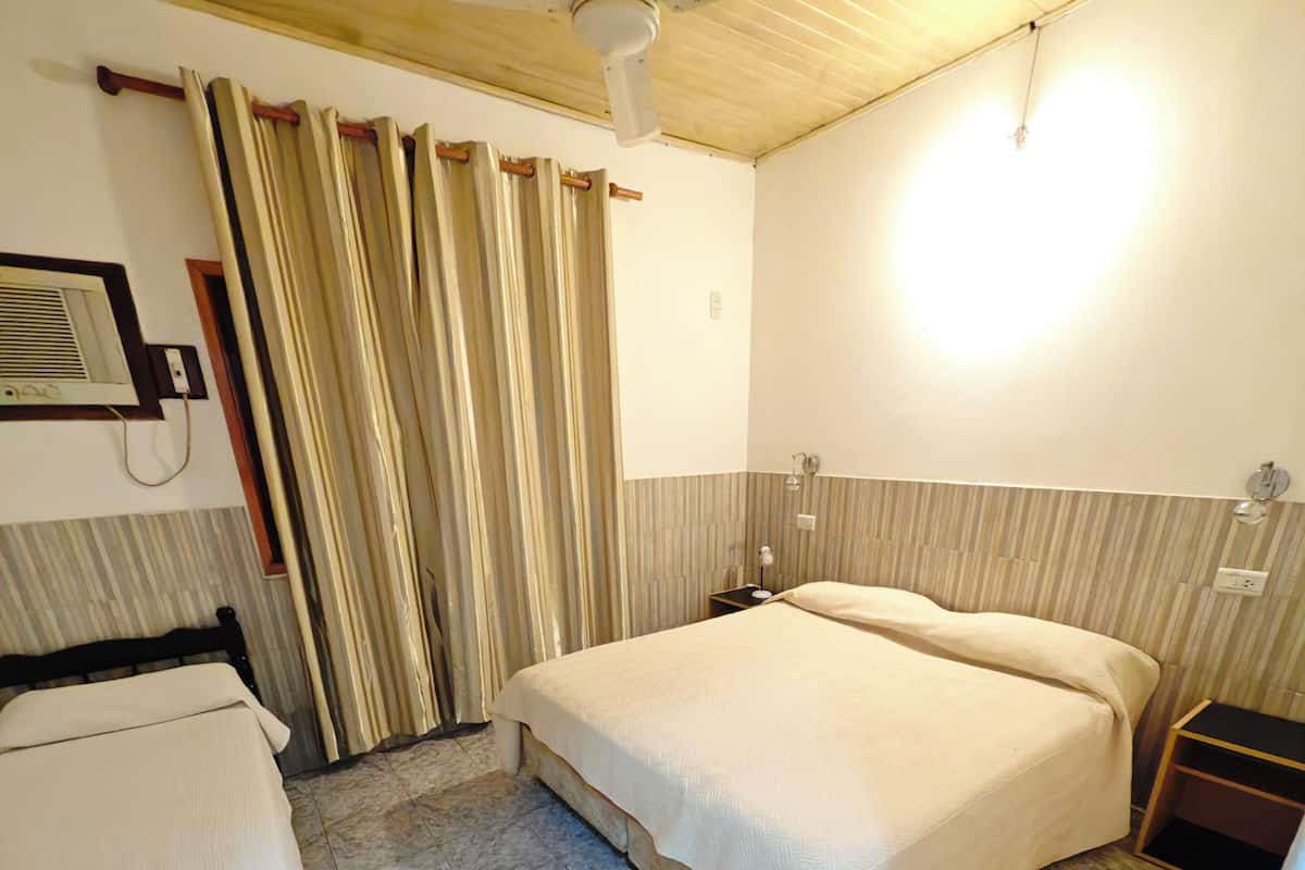 Et hotelværelse med en seng, et sengebord, en ventilator i loftet og et vindue med gardiner.