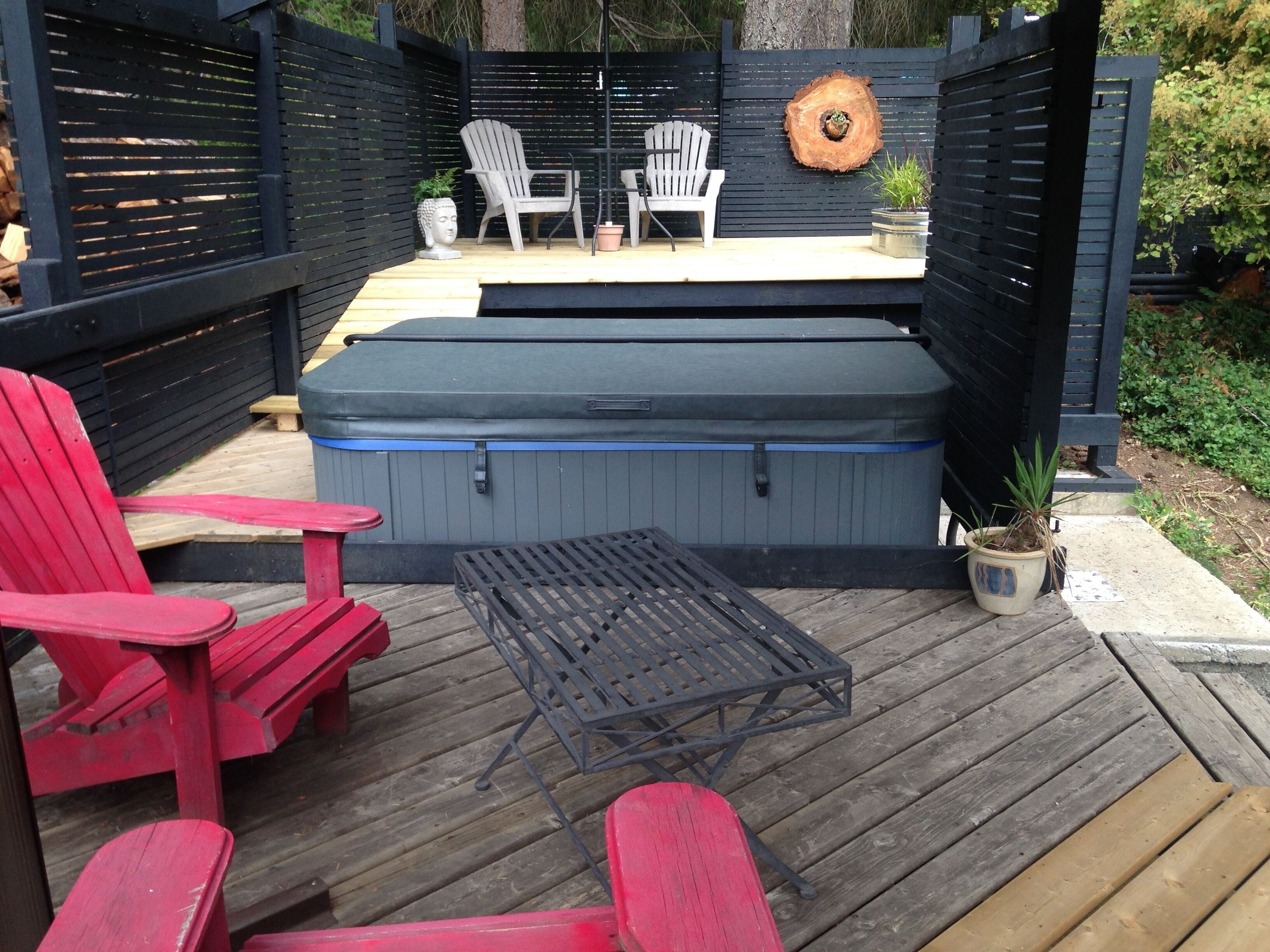 A deck with a hot tub, red chairs, and a table.