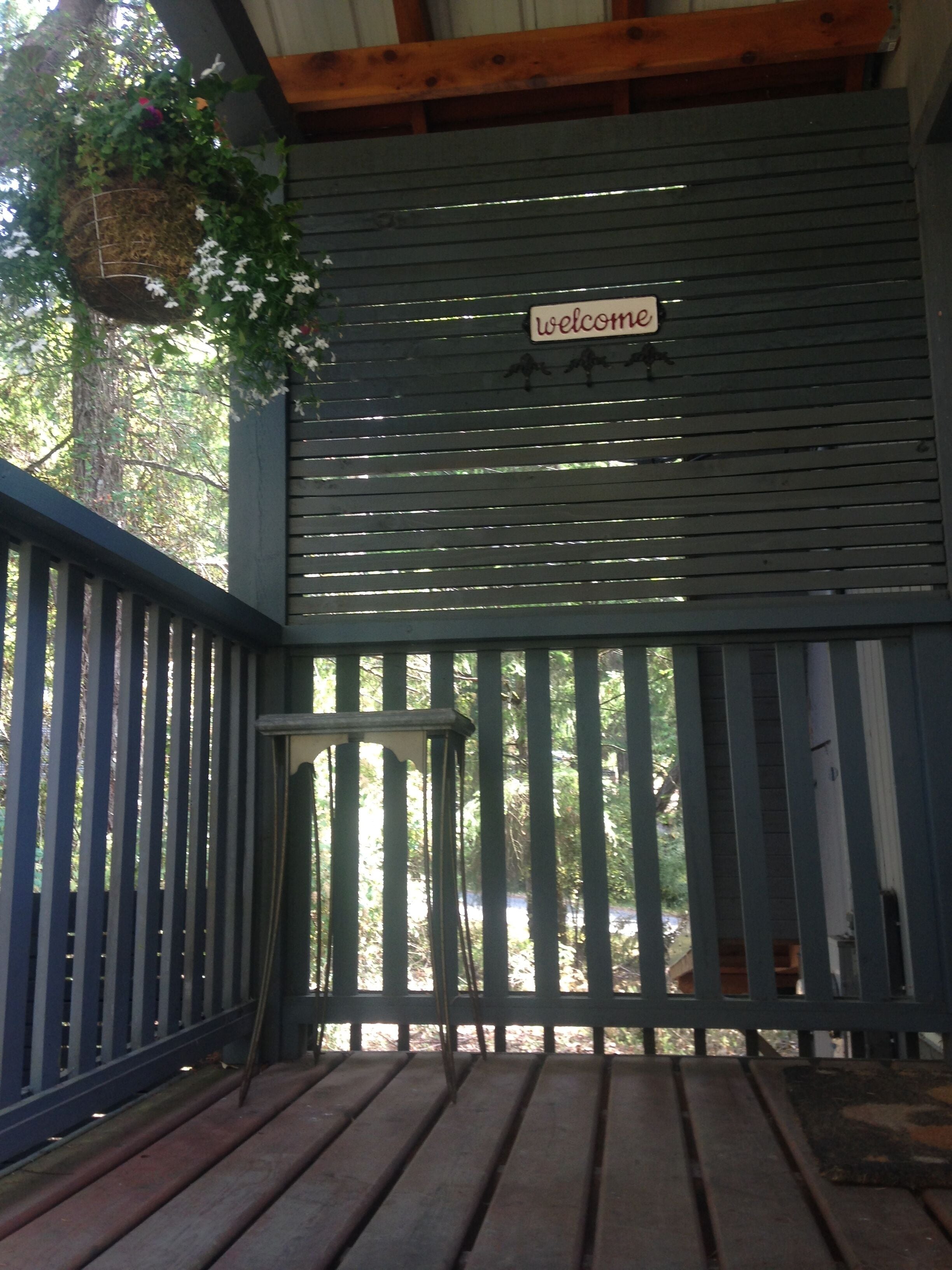 Um deck de madeira com uma placa de 'Welcome', um vaso suspenso e um guarda-corpo de metal.