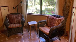 Una habitació amb dues cadires de vimetla, una taula petita, una finestra que dona als arbres i una làmpada.