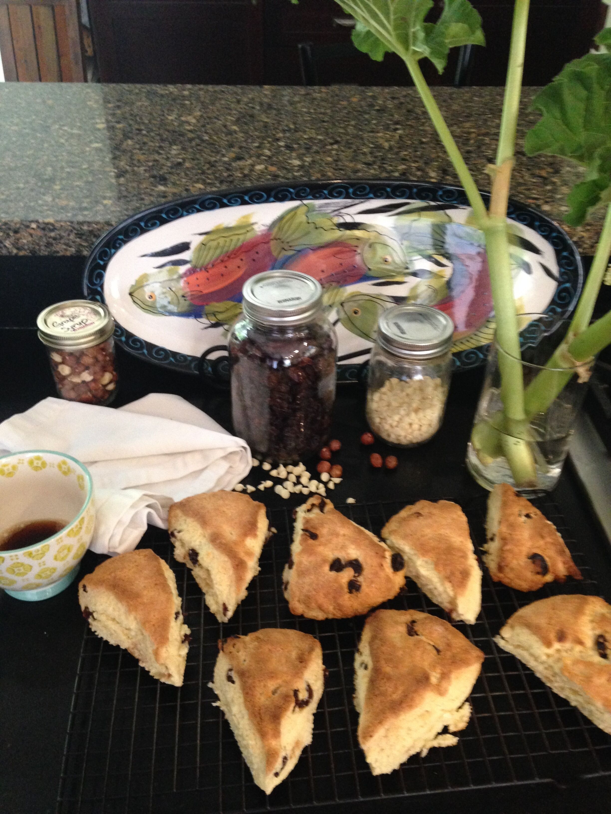 A kitchen counter with a decorative plate, jars of condiments, a cup of tea, and several scones.