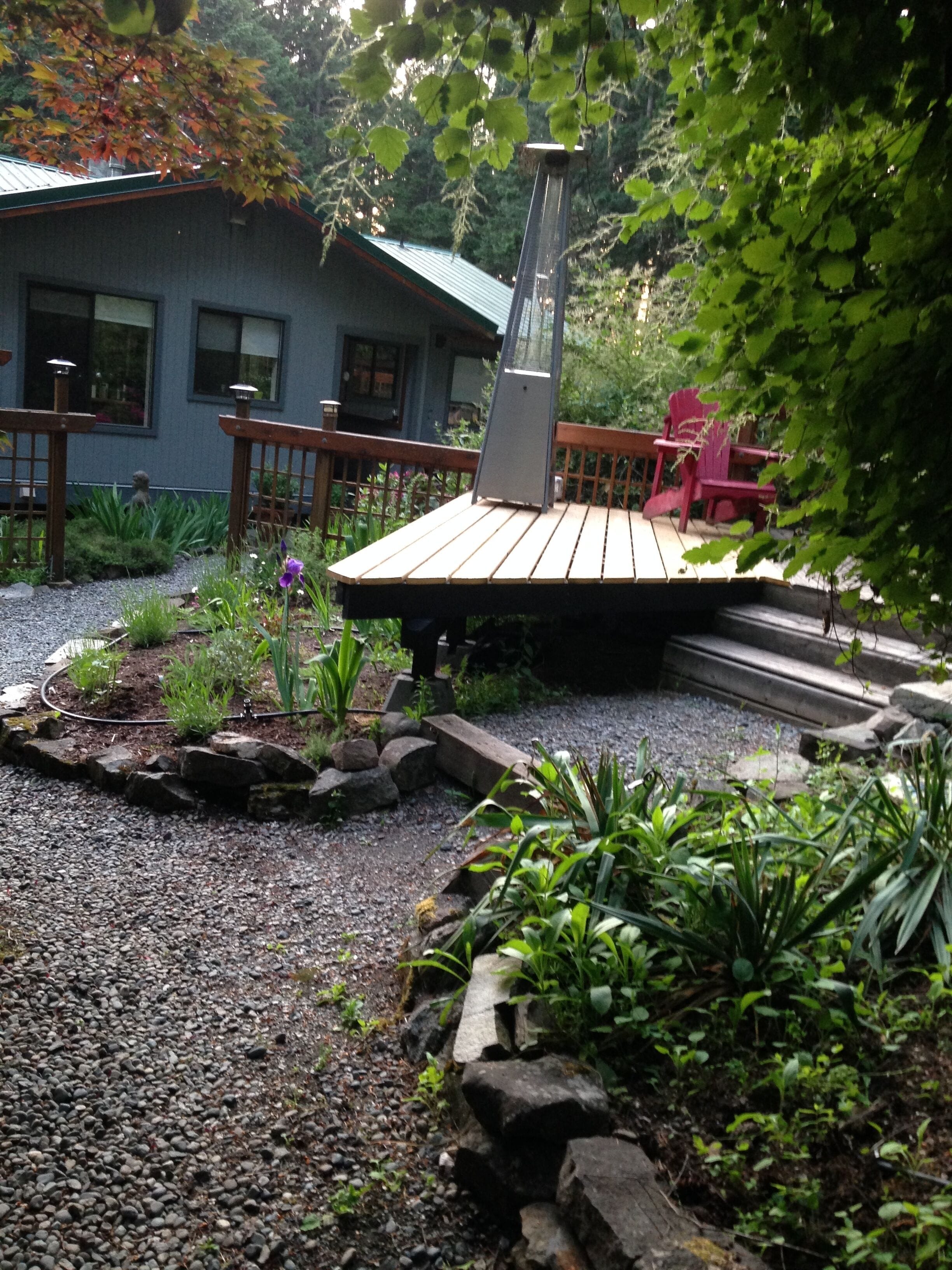 Ein Gartenbereich mit einer Holzterrasse, einem Kiesweg und verschiedenen Pflanzen.