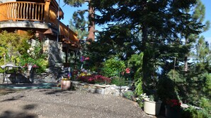 Un edificio rústico con fachada de piedra, balcón de madera y un jardín con diversas plantas y flores.