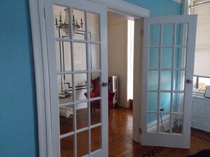 A room with a wooden floor, a red chair, a white radiator, and a window with blinds. - Serenity at Home Guest House (Brooklyn)