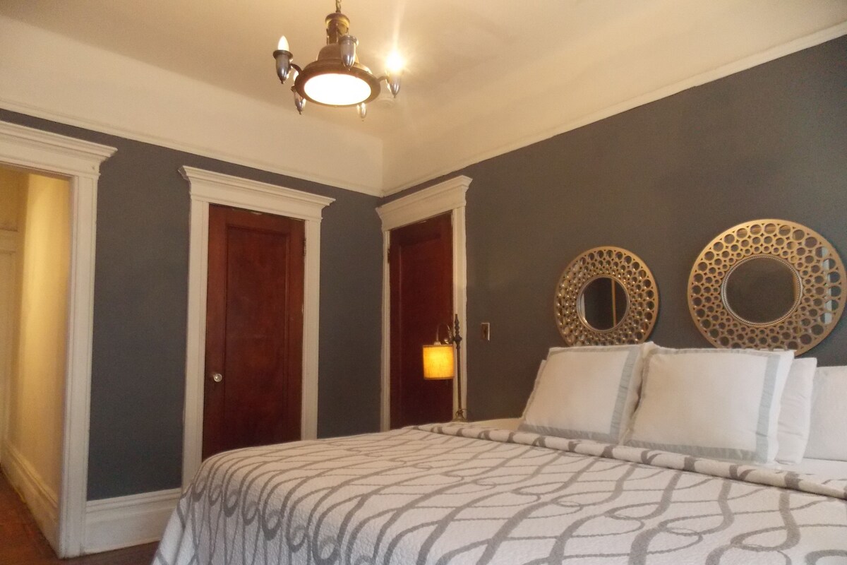 A bedroom with a large bed, two doors, and decorative wall mirrors.