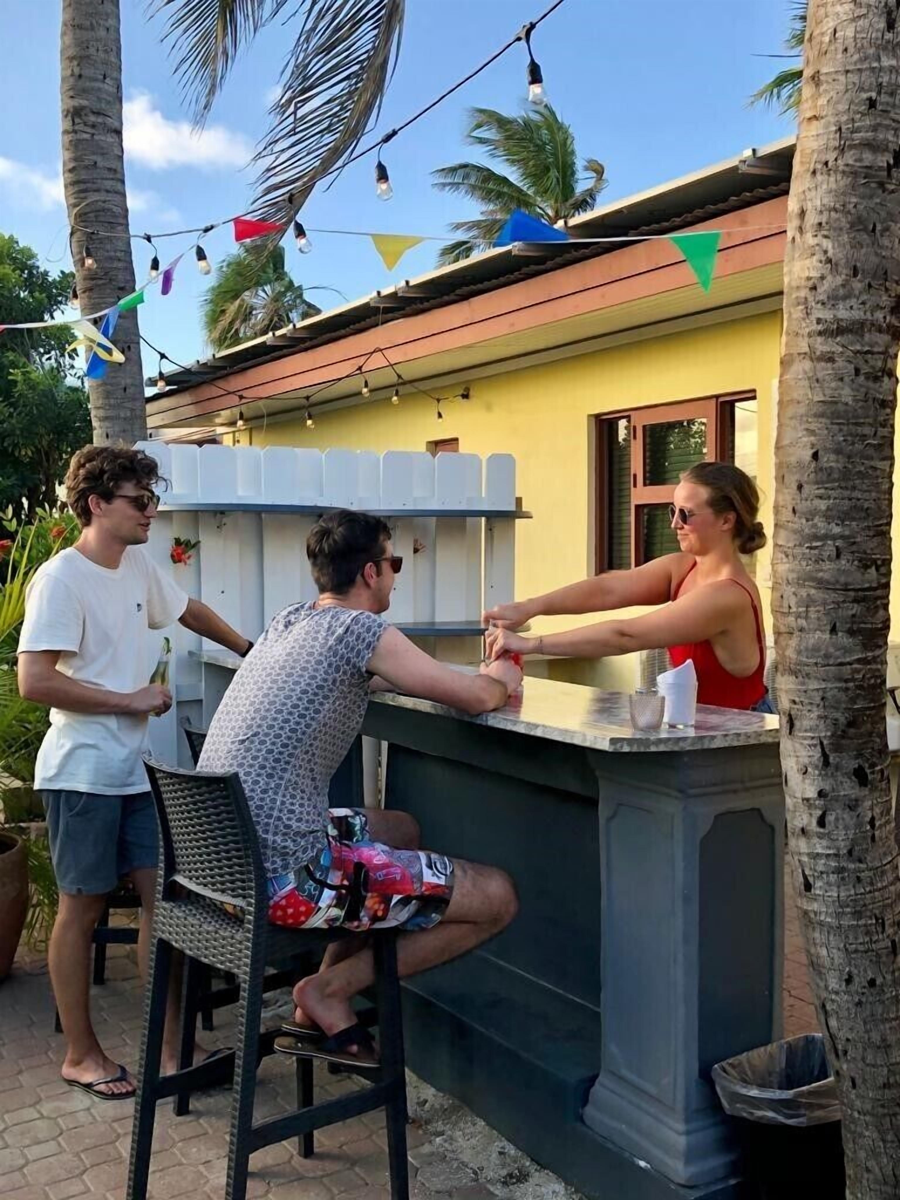 Zona de bar al aire libre con mostrador, sillas y palmeras al fondo.
