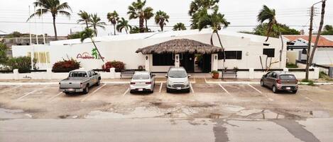 A hotel with a thatched-roof entrance, a white facade, and a parking lot with four cars.