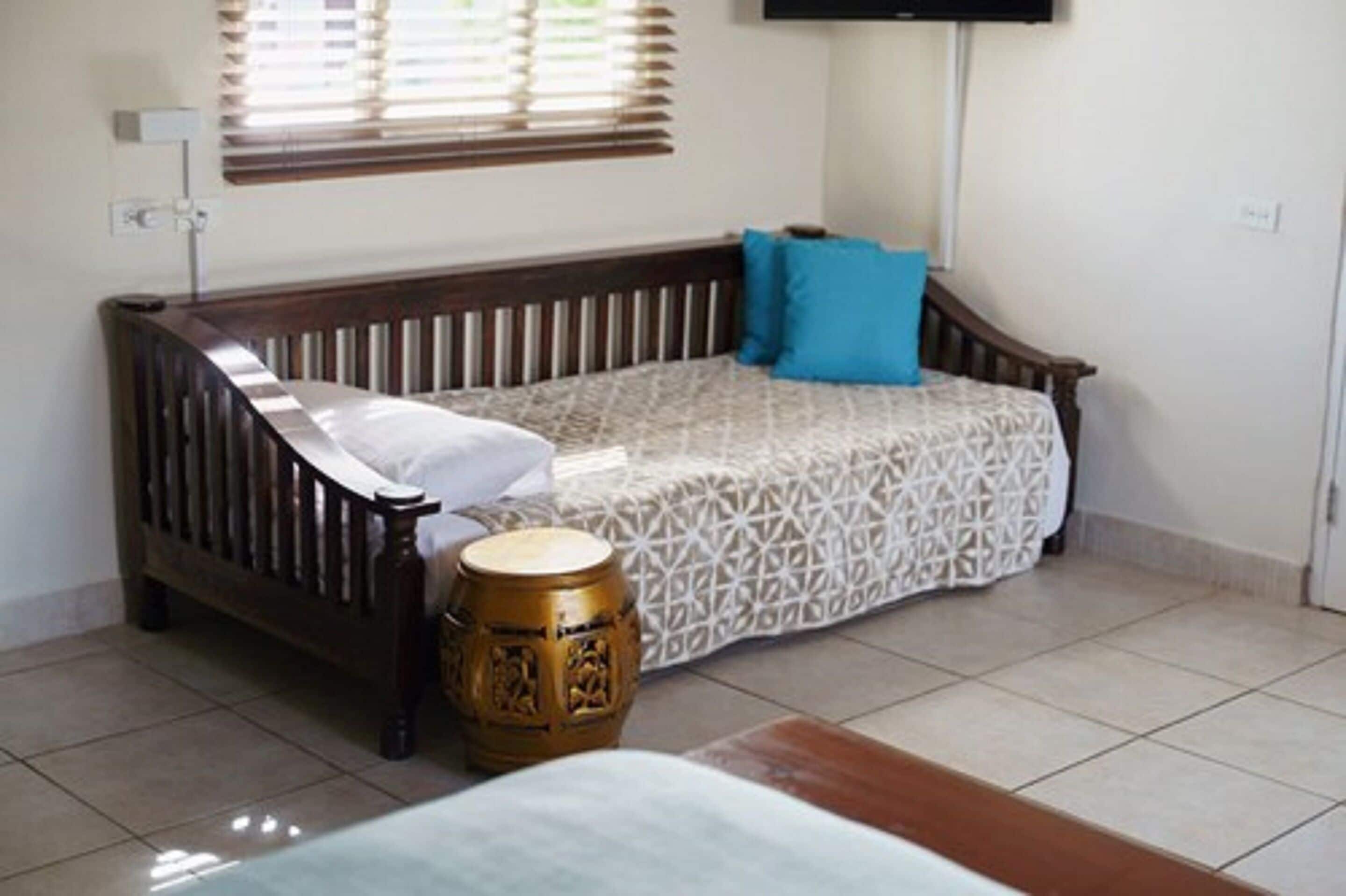 A single bed with a patterned bedspread, a blue pillow, and a wooden headboard.