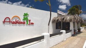 A white wall with the Arubiana Inn logo, a palm tree, and a thatched-roof building. - Arubiana Inn (Noord)