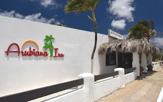 Una pared blanca con el logo del Arubiana Inn, una palmera y un edificio con techo de paja.