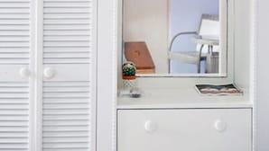 A white dresser with a mirror, a small cactus, and a picture frame. - Arubiana Inn (Noord)