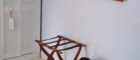 Una habitación con una silla plegable de madera, un jarrón gris y una obra de arte enmarcada en la pared.