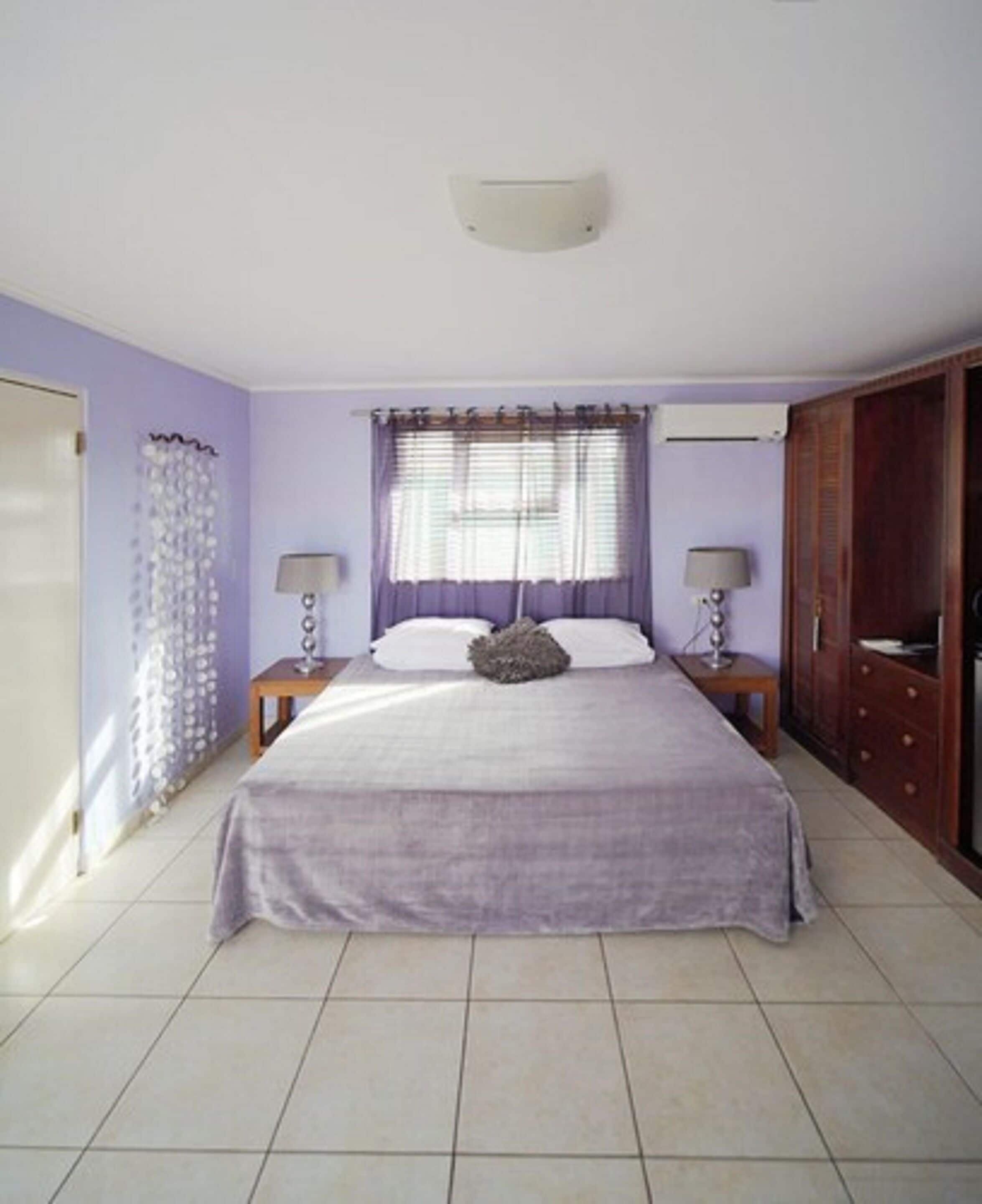 A bedroom with a bed, two bedside tables, a wardrobe, and a window with curtains.