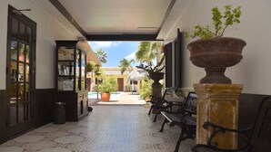A hallway with patterned floor tiles, a reception desk, a bench, and a large planter. - Arubiana Inn (Noord)