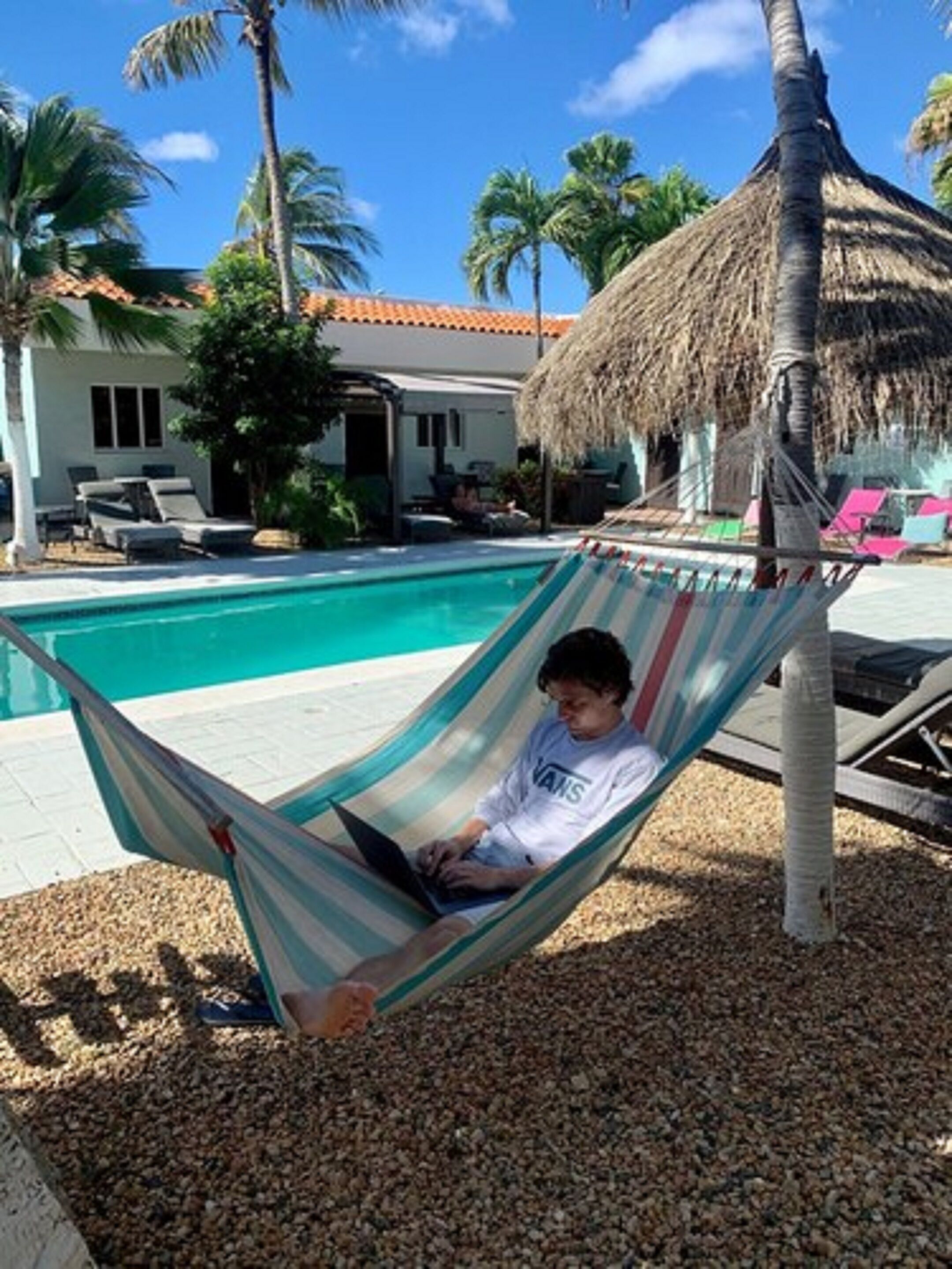 A hammock by a pool with a house in the background.