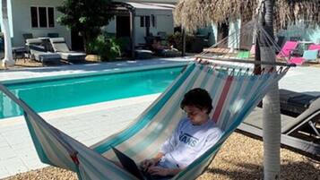 A hammock by a pool with a house in the background.