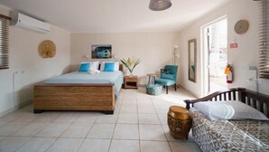 A bedroom with a large bed, a smaller bed, a chair, a small table, and a decorative basket. - Arubiana Inn (Noord)