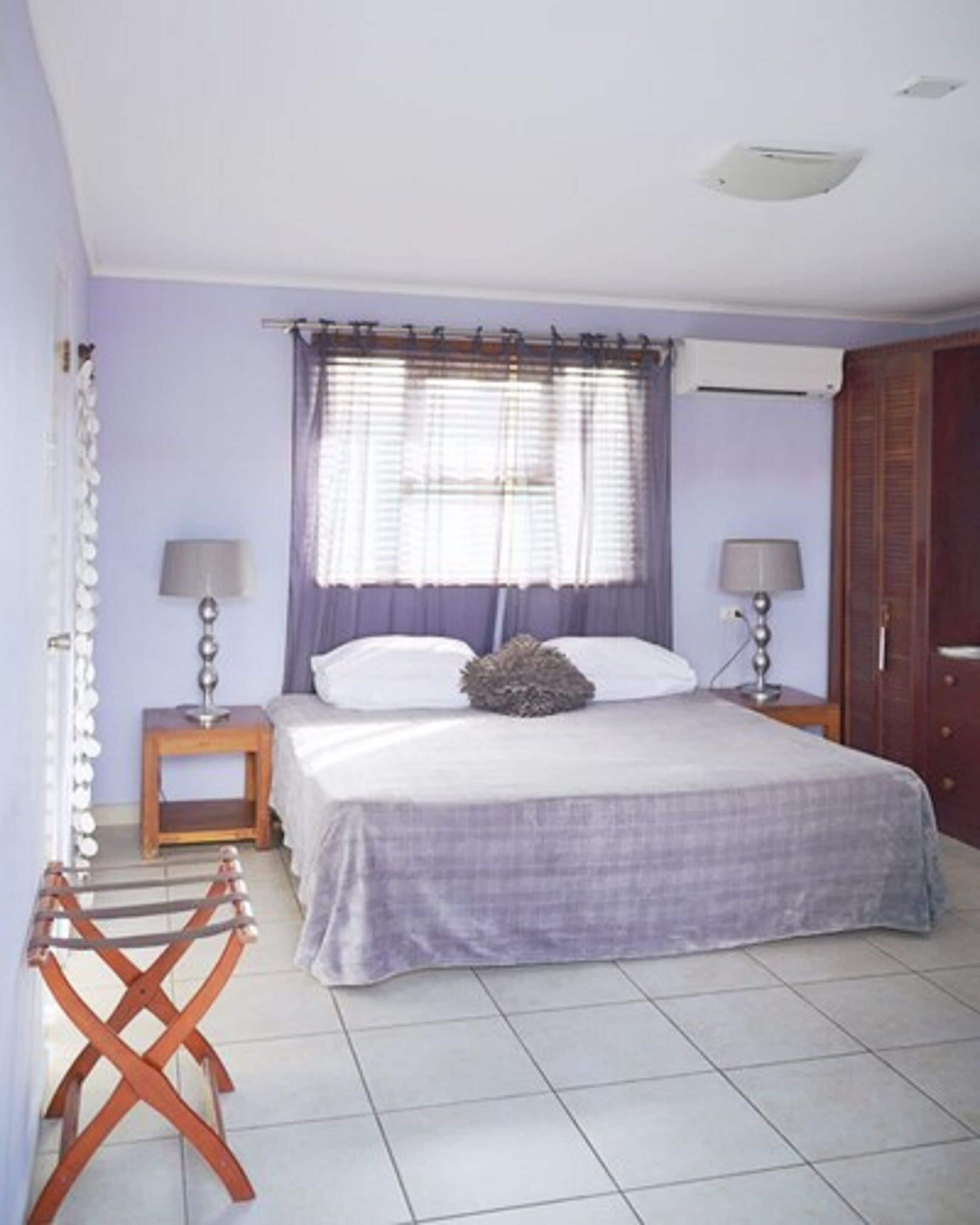 Un dormitorio con una cama, dos mesitas de noche con lámparas, una ventana con cortinas y una puerta.