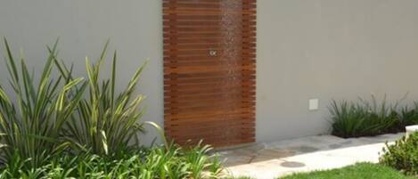 A modern outdoor shower with a wooden panel design, surrounded by a well-maintained garden with various plants.