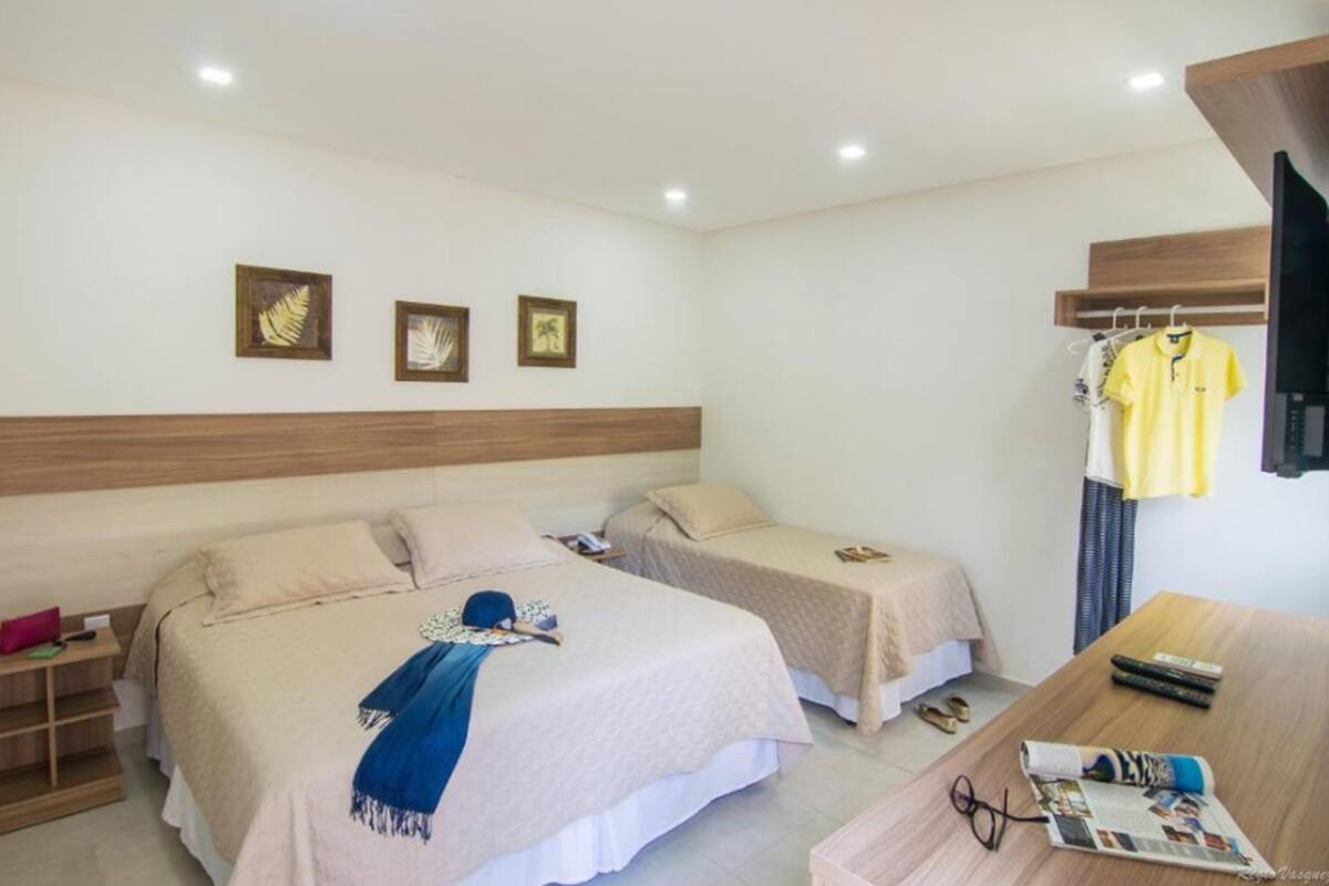 A hotel room with two beds, a wooden headboard, a TV, a table with a magazine, and a hanging rack with clothes.