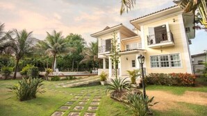 A two-story house with a garden, palm trees, and a stone pathway.