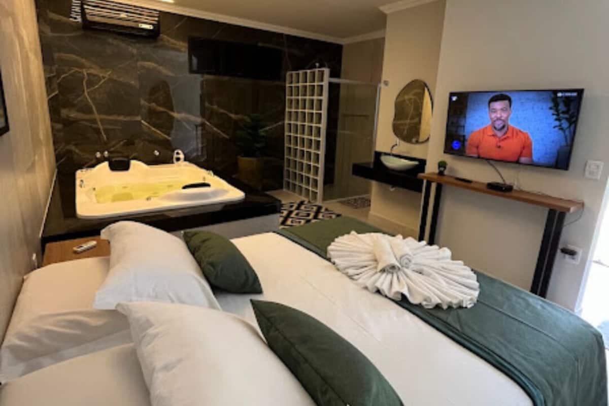 A modern hotel room with a large bed, a TV, a bathtub, and a shower area.