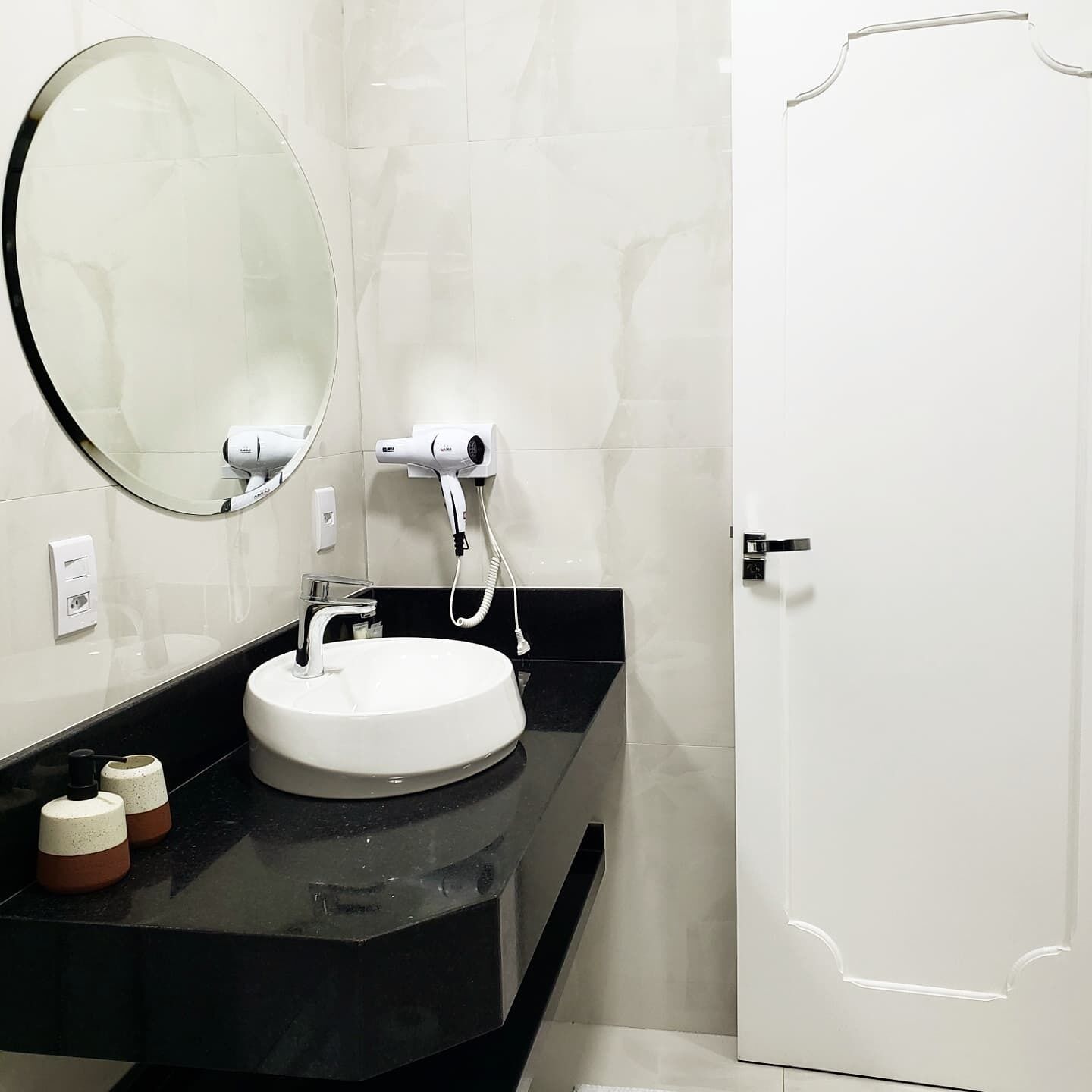 A modern bathroom with a round mirror, a white sink, and a hairdryer on a black countertop.