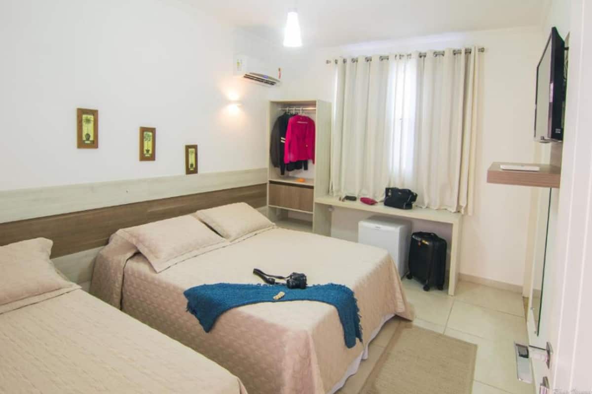 A hotel room with two beds, a wardrobe, a desk with a chair, a television, and a window with curtains.