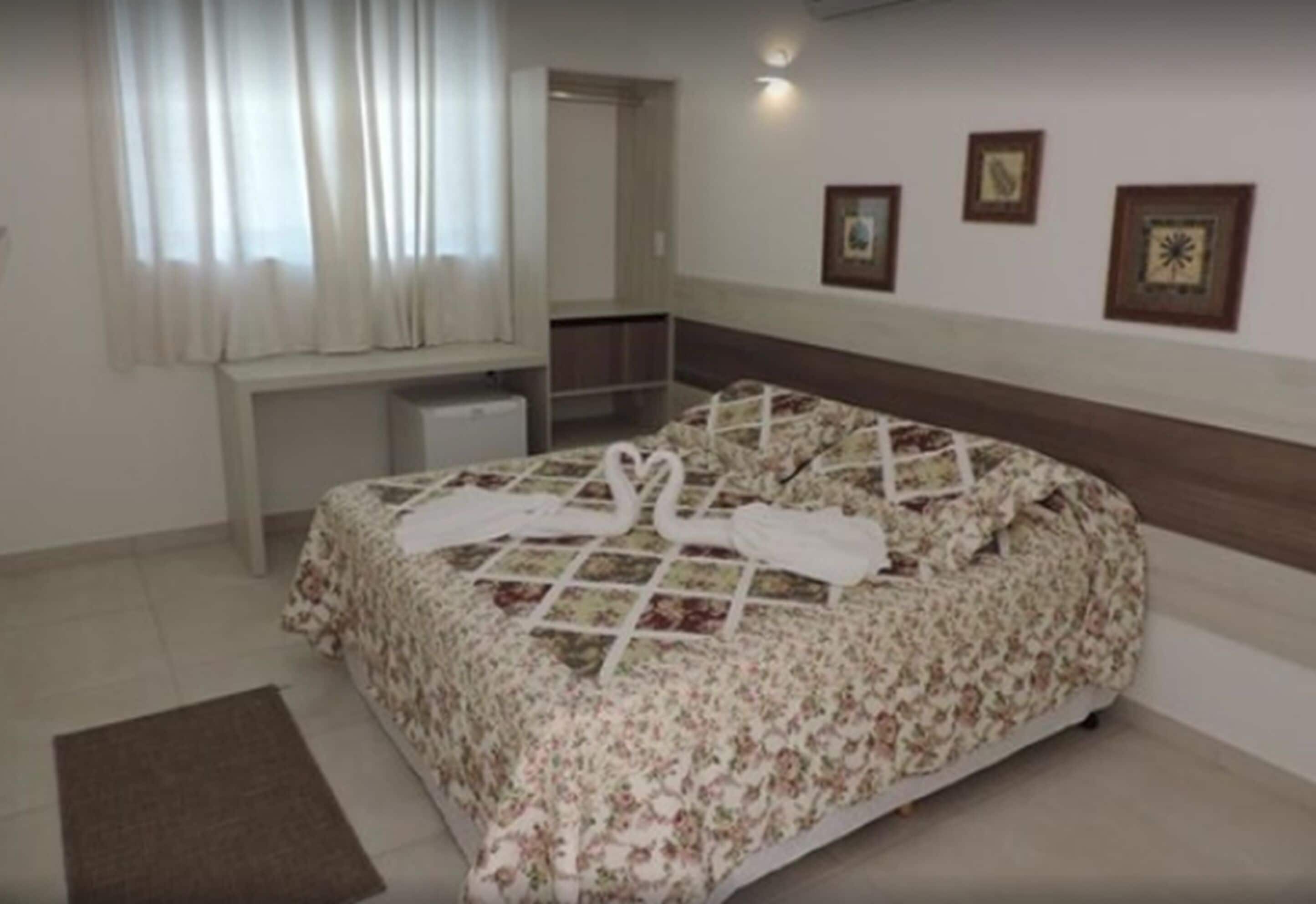 A bedroom with a bed, a bedside table, a mirror, and a window with curtains.