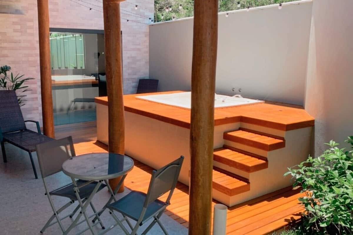 A modern outdoor seating area with a wooden bench, a round table, and a hot tub.