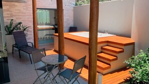 A modern outdoor seating area with a wooden bench, a round table, and a hot tub.