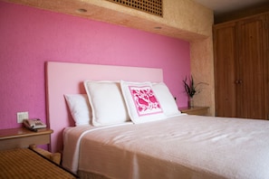 A bedroom with a pink wall, a wooden headboard, a bed with white bedding, a bedside table with a phone, and a wooden wardrobe.